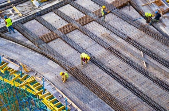 Workers in yellow helmets and vests constructing a fire-safe metal structure on a construction site, emphasizing safety and fire prevention in building practices.