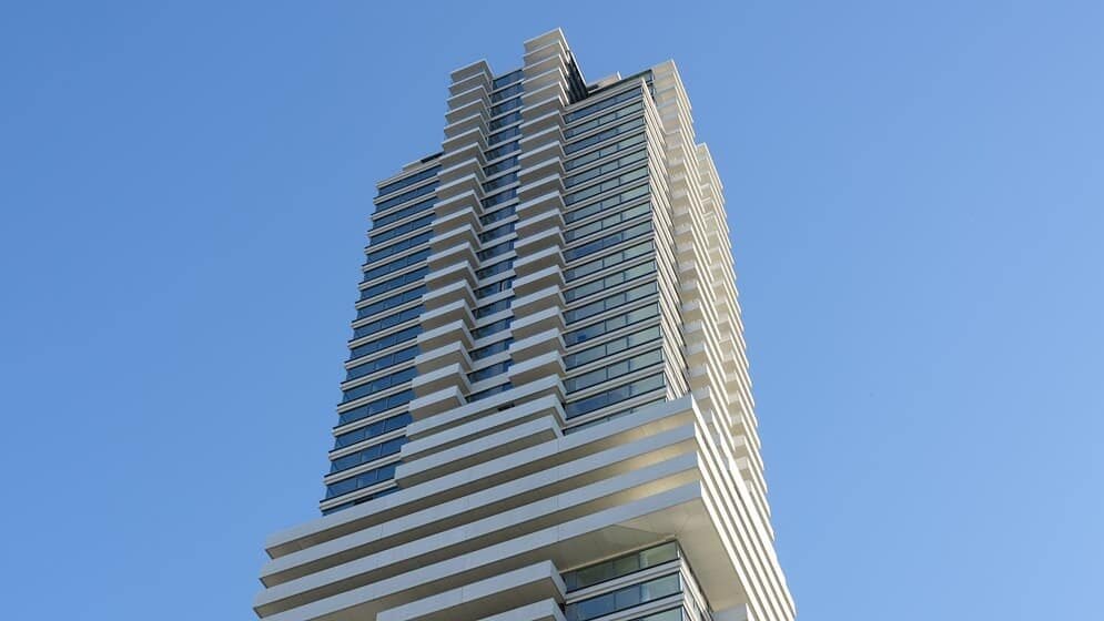 Moderne toren met glazen gevel en brandwerende elementen, ontworpen voor veiligheid en esthetiek, tegen een heldere lucht achtergrond.