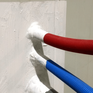 Rode en blauwe buizen tegen een brandwerende wand, illustrerend het proces van brandwerend maken van staalconstructies.